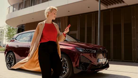 My BMW App My BMW App Woman on street with smartphone in hand and BMW vehicle in background