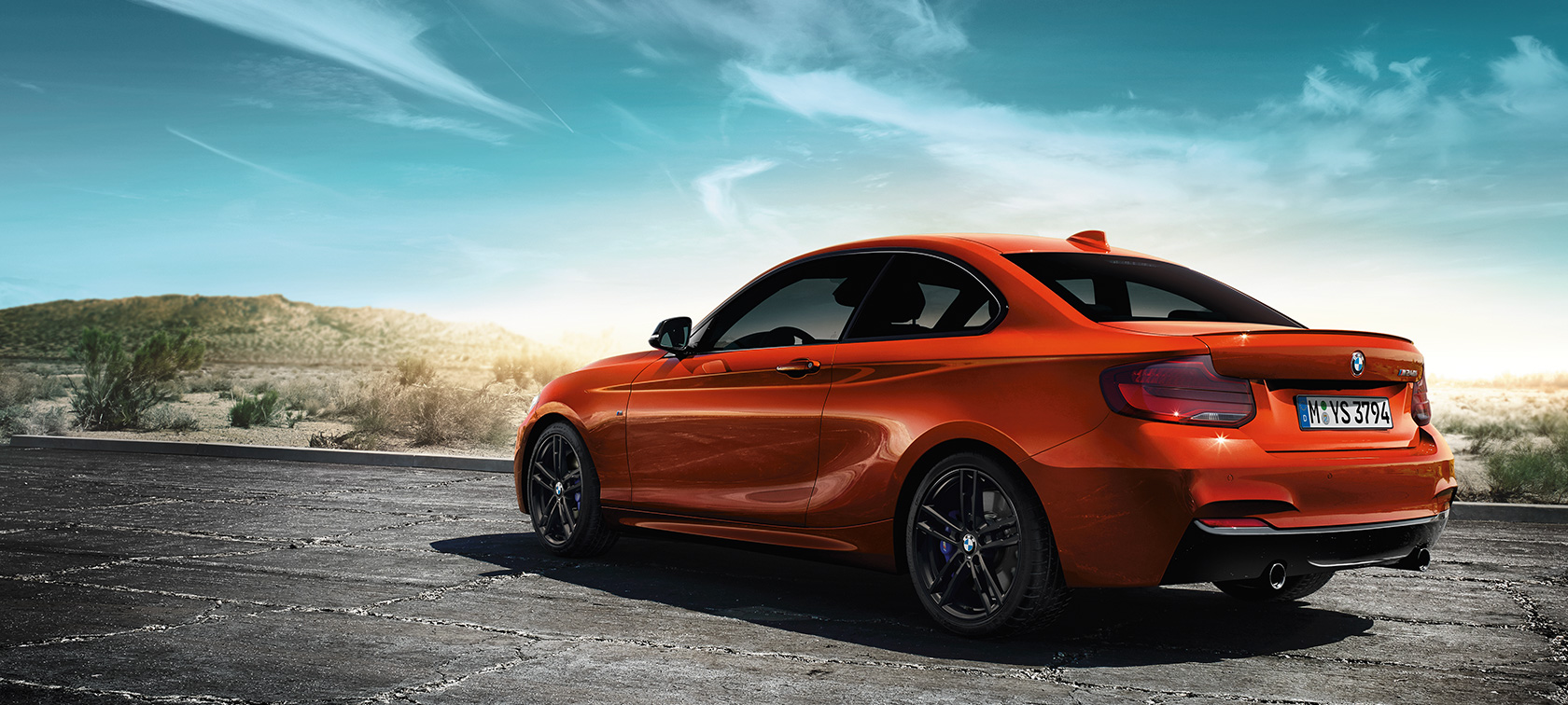 BMW M240i Coupé F22 2017 three-quarter rear view BMW M240i Coupé F22 2017 Sunset Orange metallic three-quarter rear view standing in front of steppe landscape