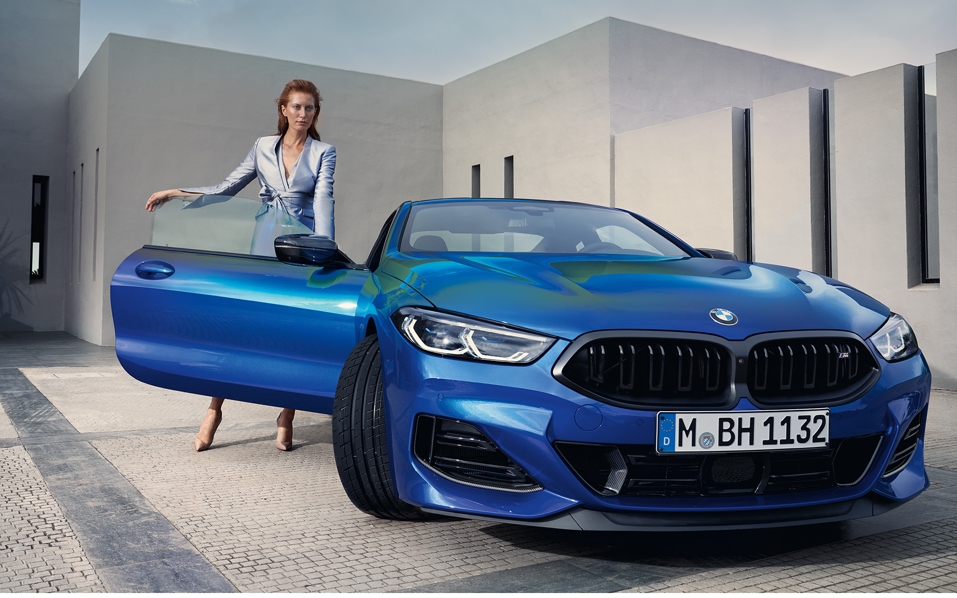 BMW M850i xDrive Coupé G15 LCI Facelift 2022 front view standing BMW M850i xDrive Coupé G15 LCI Facelift 2022 M Portimao Blue metallic front view standing with female model in open front door