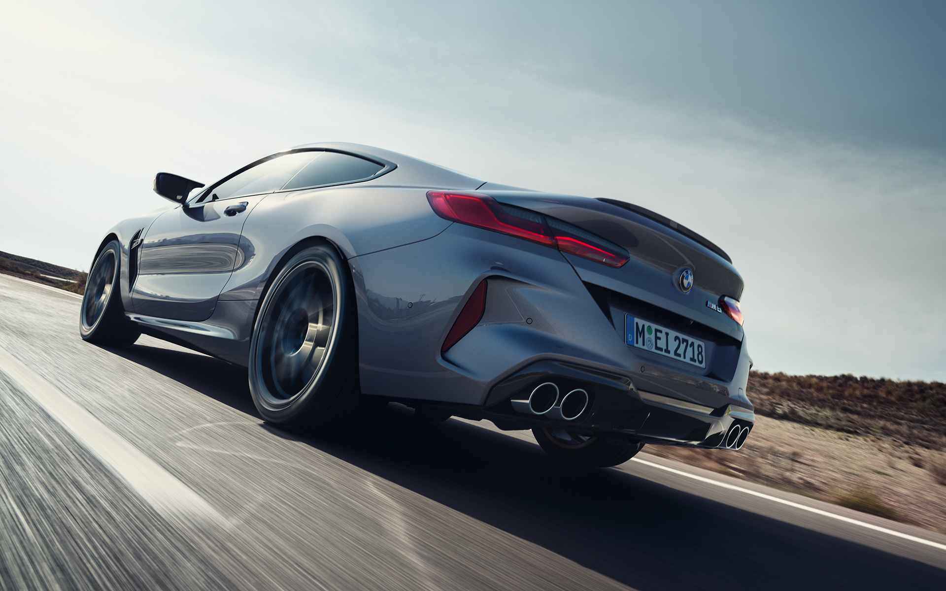 Three-quarter rear view BMW M8 Coupé F92 LCI Facelift 2022 driving on a highway BMW M8 coupe F92 LCI facelift 2022 Skyscraper grey metallic three-quarter rear view driving on a highway low angle shot