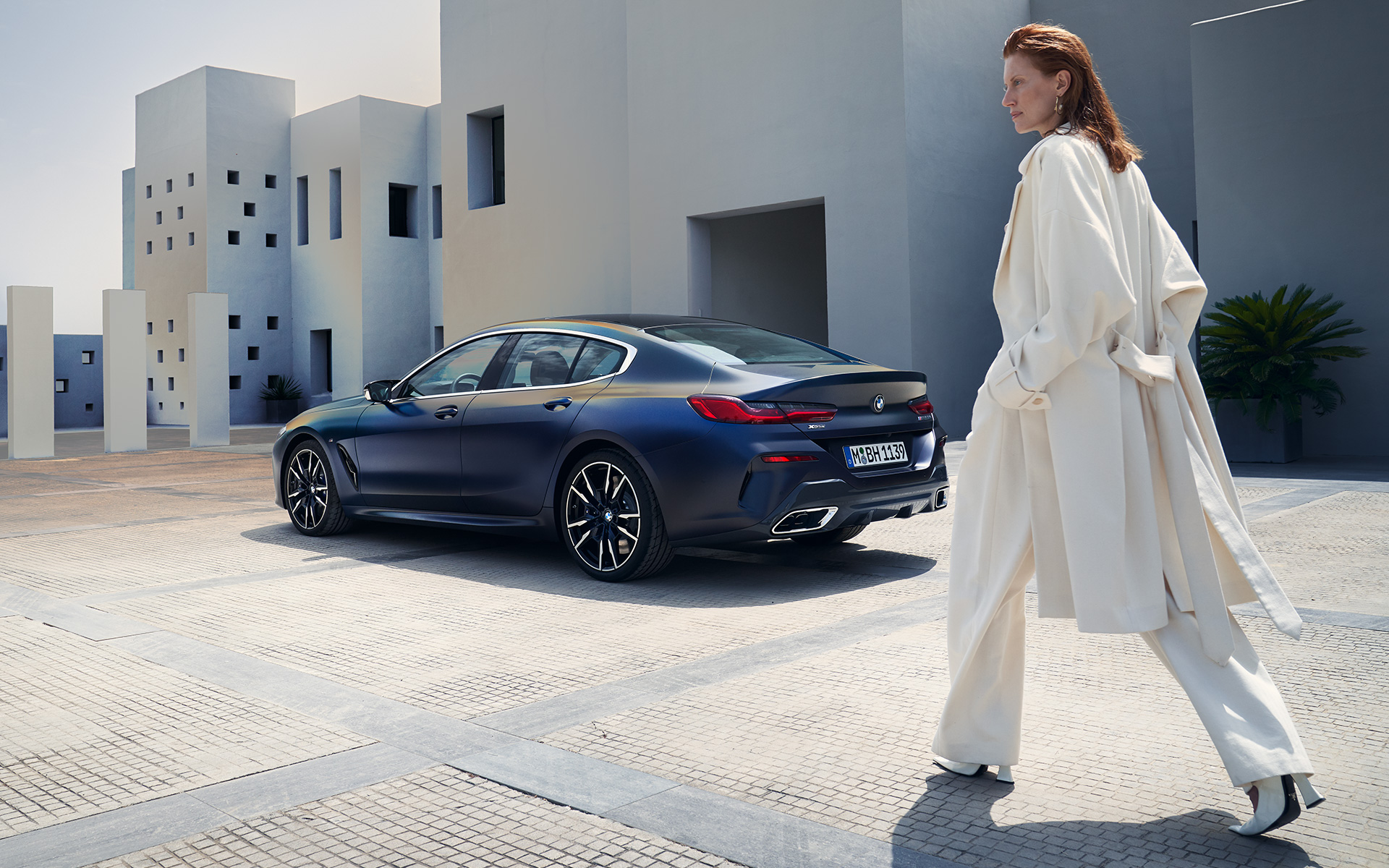 BMW M850i xDrive Gran Coupé G16 LCI Facelift 2022 side view with female model BMW M850i xDrive Gran Coupé G16 LCI Facelift 2022 BMW Individual Frozen Tanzanite Blue metallic three-quarter rear view with female model