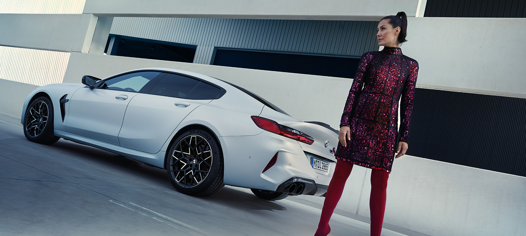 Three-quarter rear view BMW M8 Competition Gran Coupé F93 LCI 2022 BMW M8 Competition Gran Coupé F93 LCI Facelift 2022 BMW Individual Frozen Brilliant White metallic three-quarter rear view with female model standing next to vehicle