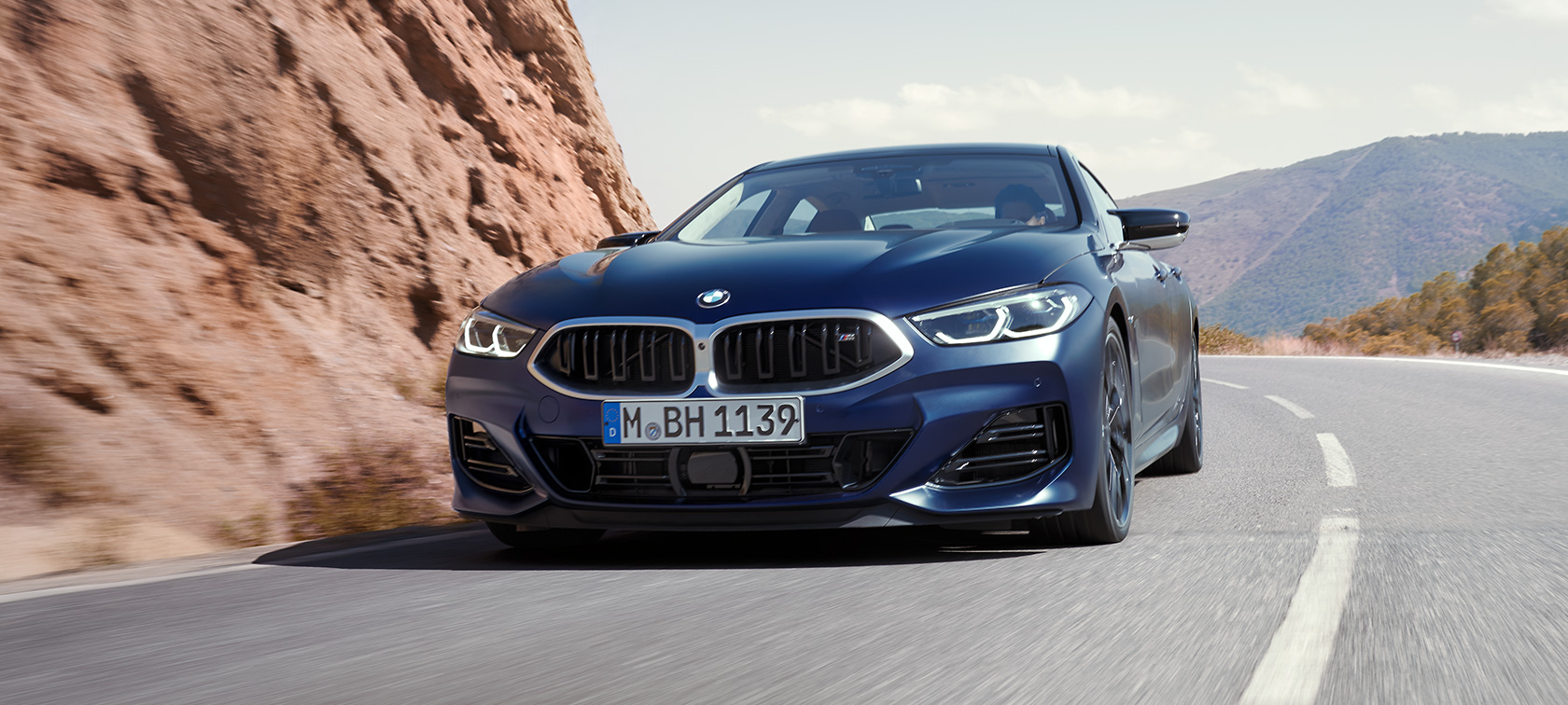 Three-quarter front view driving BMW M850i xDrive Gran Coupé G16 LCI Facelift 2022 BMW M850i xDrive Gran Coupé G16 LCI Facelift 2022 BMW Individual Frozen Tanzanite Blue metallic three-quarter front view driving through the bend