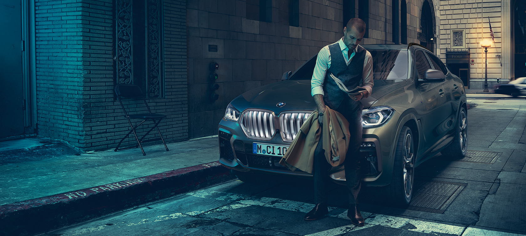 Man leaning on BMW X6. Man leaning on BMW X6 in lateral perspective in front of an urban setting.