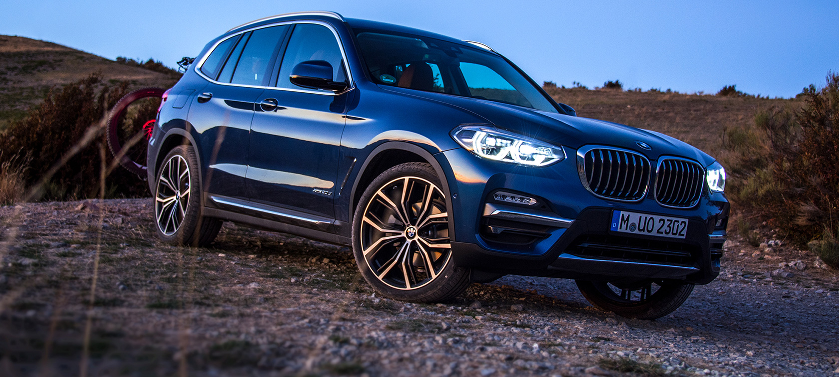 Dark blue BMW X3 in open terrain Dark blue BMW X3 parked with carrier and mountain bike on open terrain