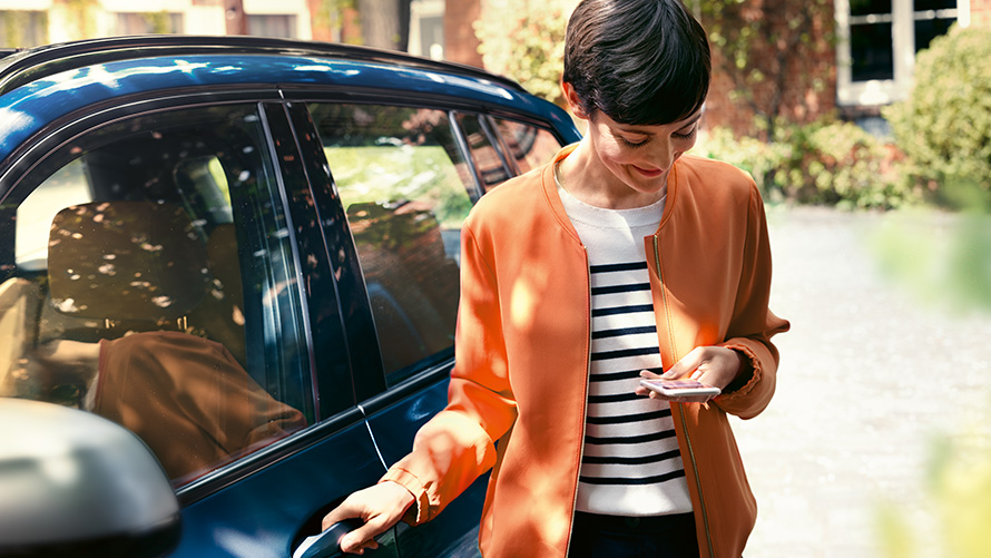 BMW Teleservices Woman with smartphone stands at the door of her BMW