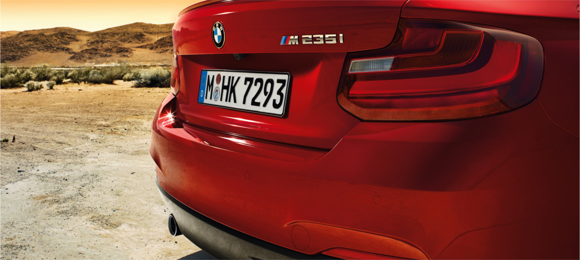 BMW M235i – Rear Design and Signature M Performance Styling Rear view of a red BMW M235i parked in a desert setting, showcasing the vehicle’s sporty M badge and performance design