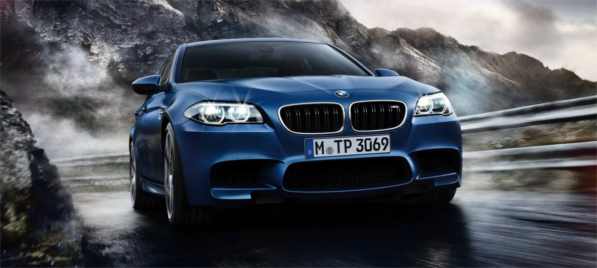 BMW M5 – High-Performance Sedan with Adaptive M Suspension for Alpine Roads Blue BMW M5 driving through a winding alpine road with mist and mountains in the background, highlighting agility and precision handling