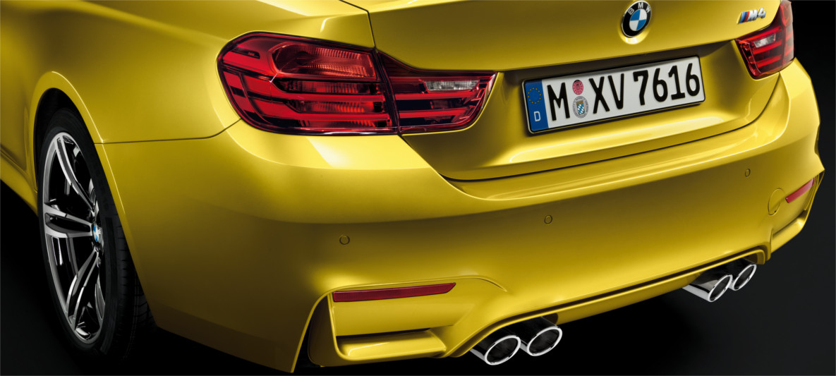 Close-up rear view of a yellow BMW M4 showcasing quad exhaust tips, M badging, and aerodynamic rear diffuser