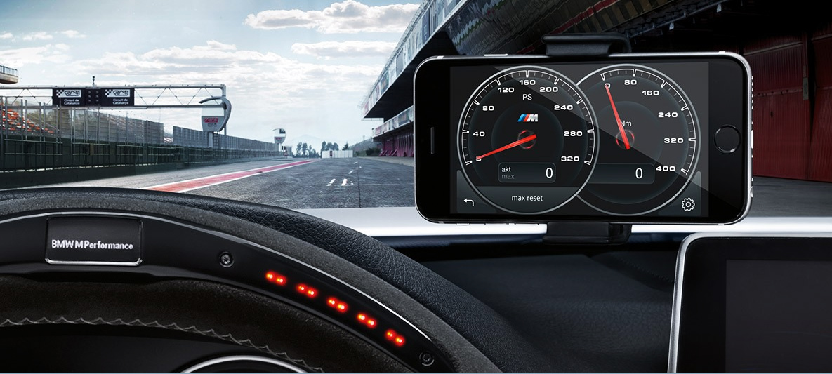BMW M Performance Parts – Track-Focused Cockpit with Telemetry Display and Sport Steering Wheel BMW M Performance Parts cockpit view featuring a performance steering wheel and smartphone telemetry display on a racetrack